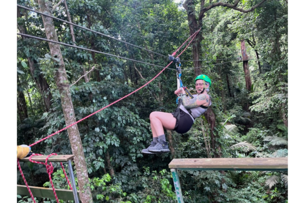 Justine is pictured riding a zipline through a wooded area.